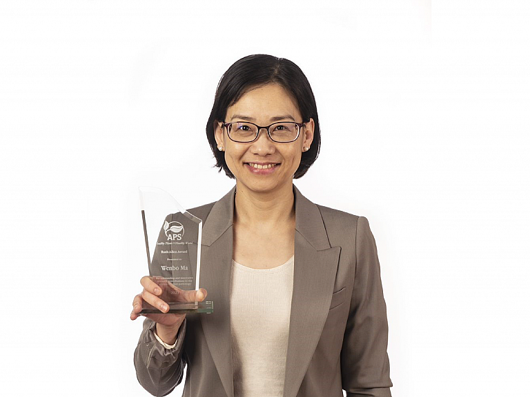 Photograph of Wenbo Ma against a white background. Wenbo is holding the Ruth Allen Award trophy in her right hand.